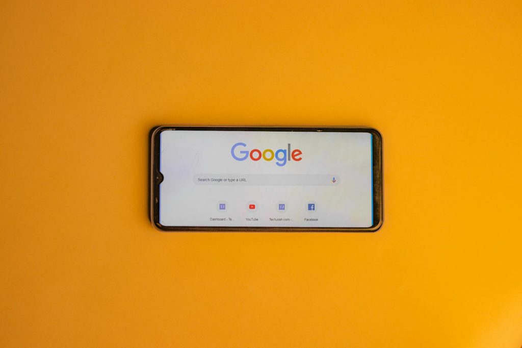 Smartphone displaying Google search page on a vibrant yellow background.