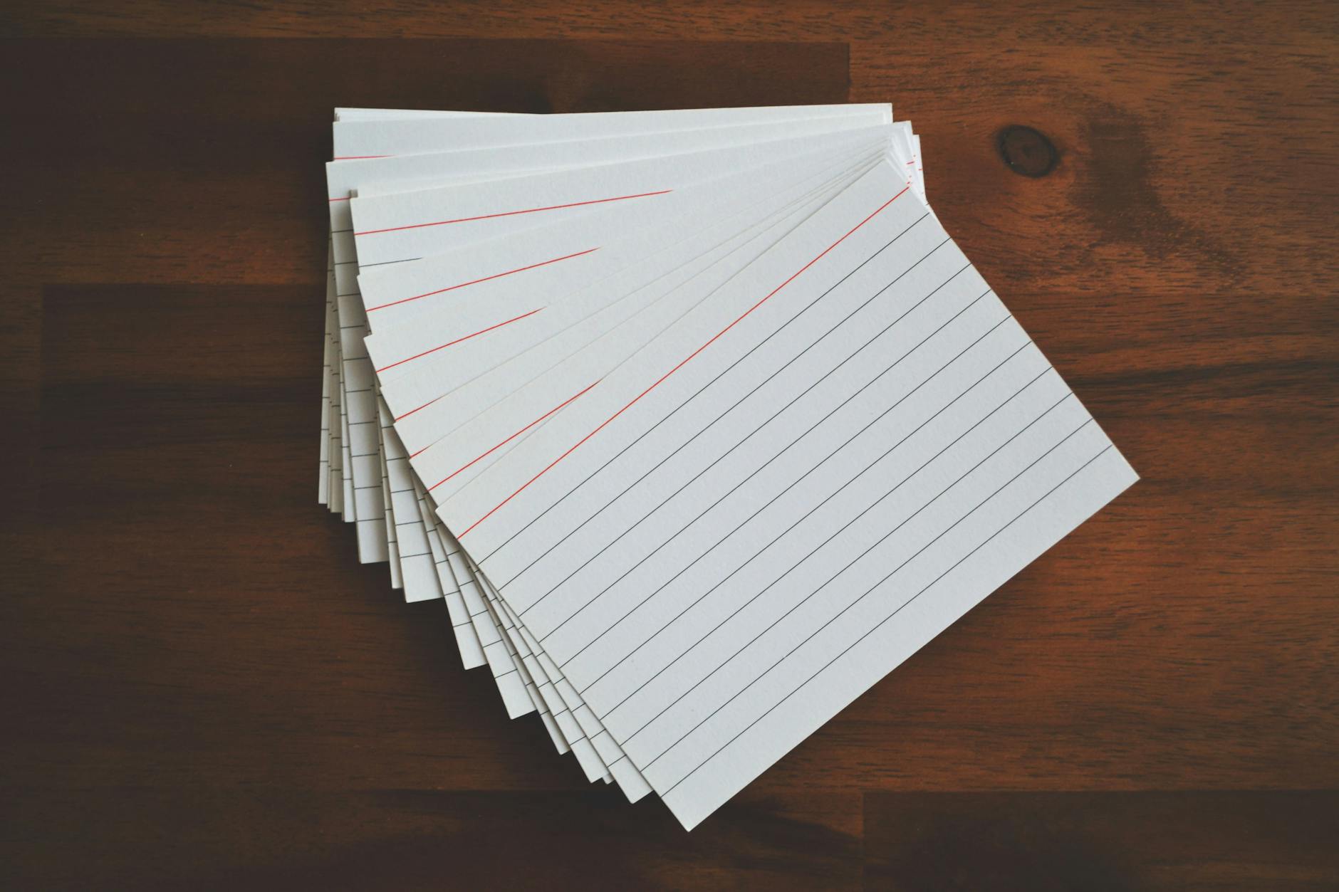 High-angle view of blank index cards arranged neatly on a wooden desk, ideal for education and organization concepts.