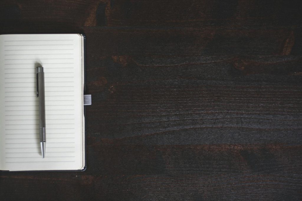A minimalist open notebook with a pen on a dark wooden desk offering ample copyspace.