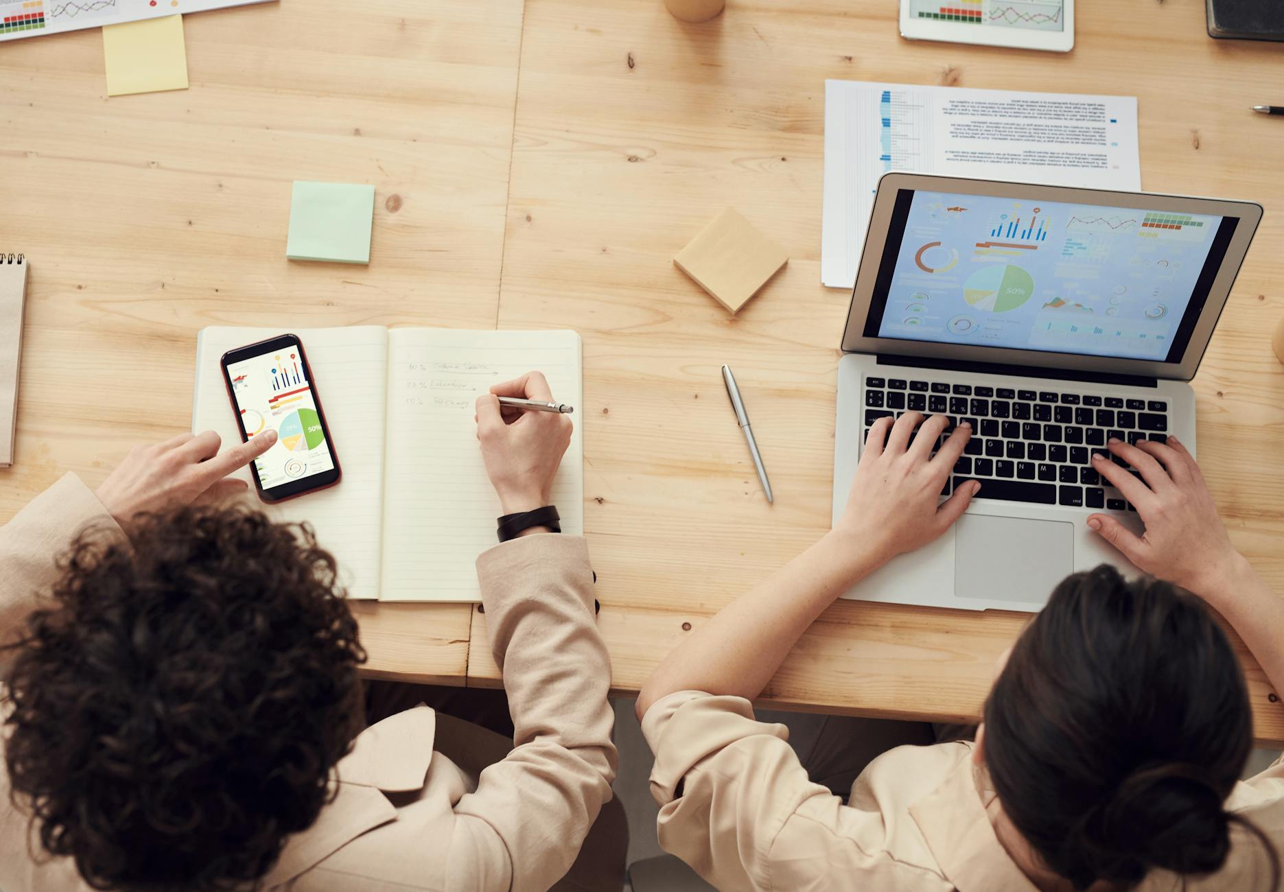 Overhead shot of two colleagues collaborating with devices and notes in a business meeting.