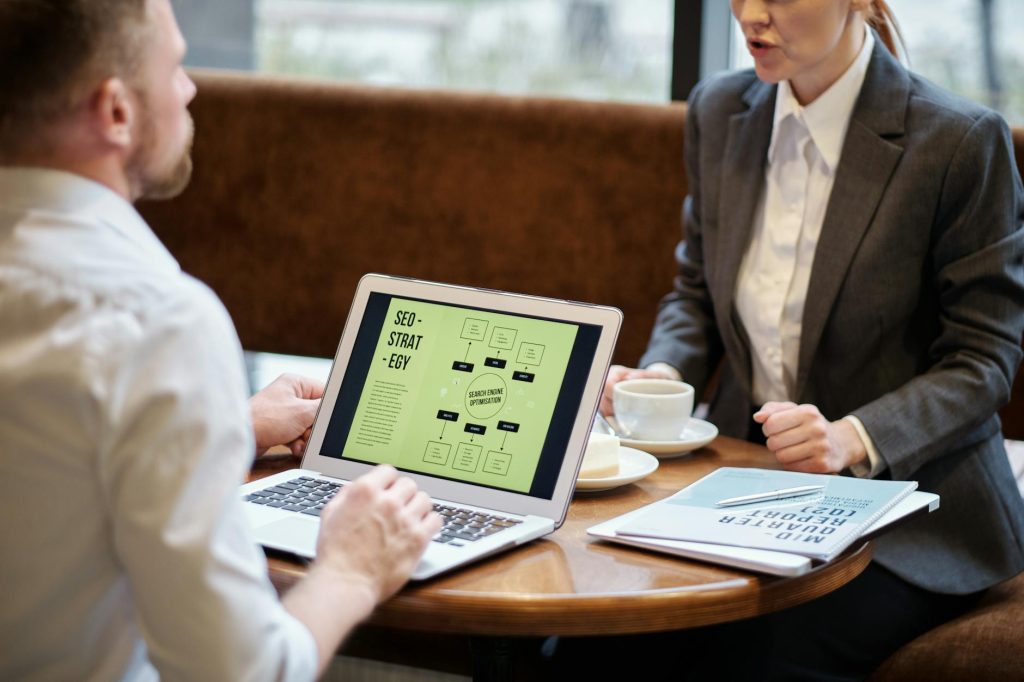 A man and woman engaged in a business meeting discussing SEO strategy in a cozy cafe setting.
