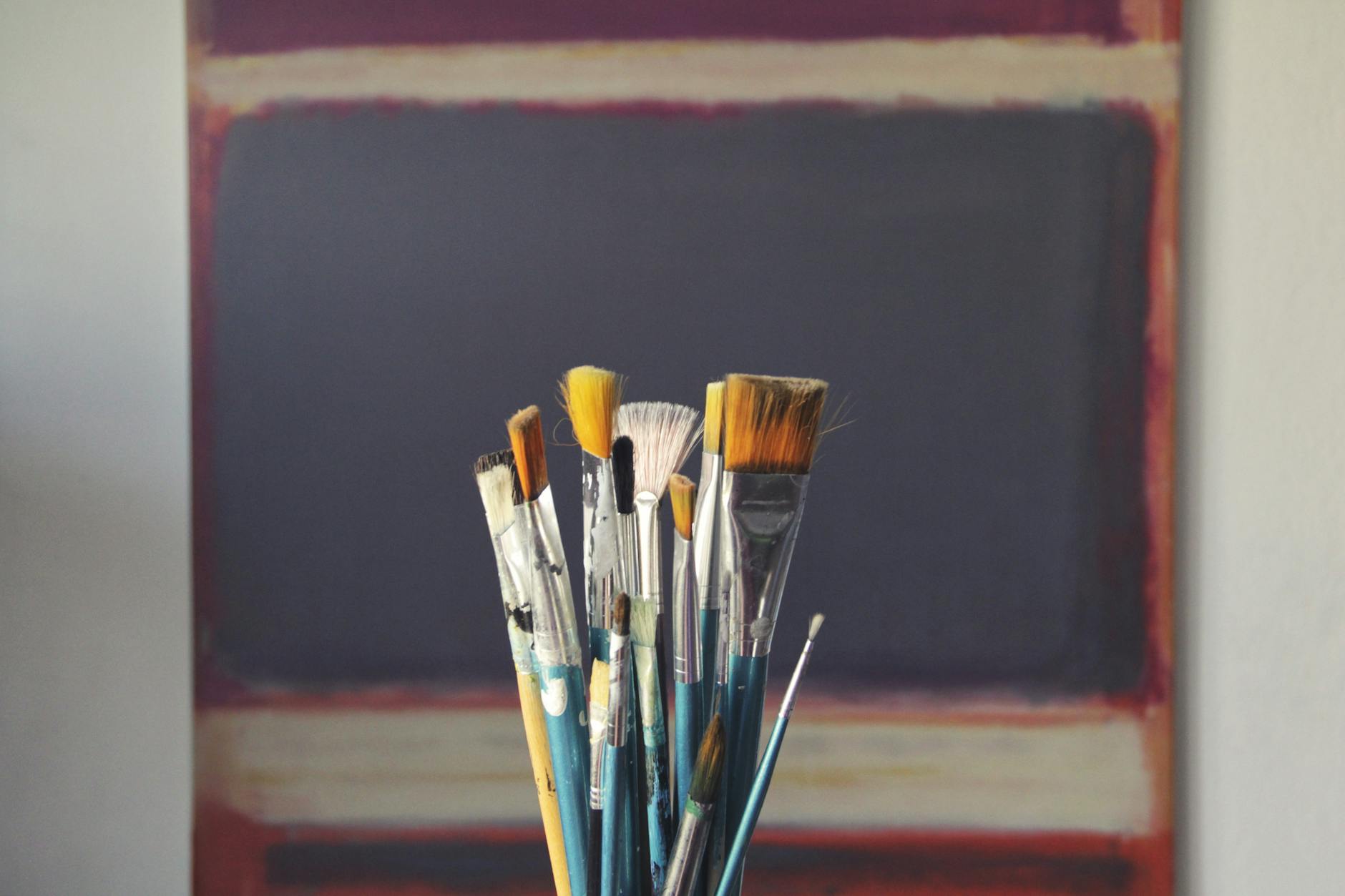A set of paintbrushes in front of an abstract canvas, reflecting creativity and inspiration.