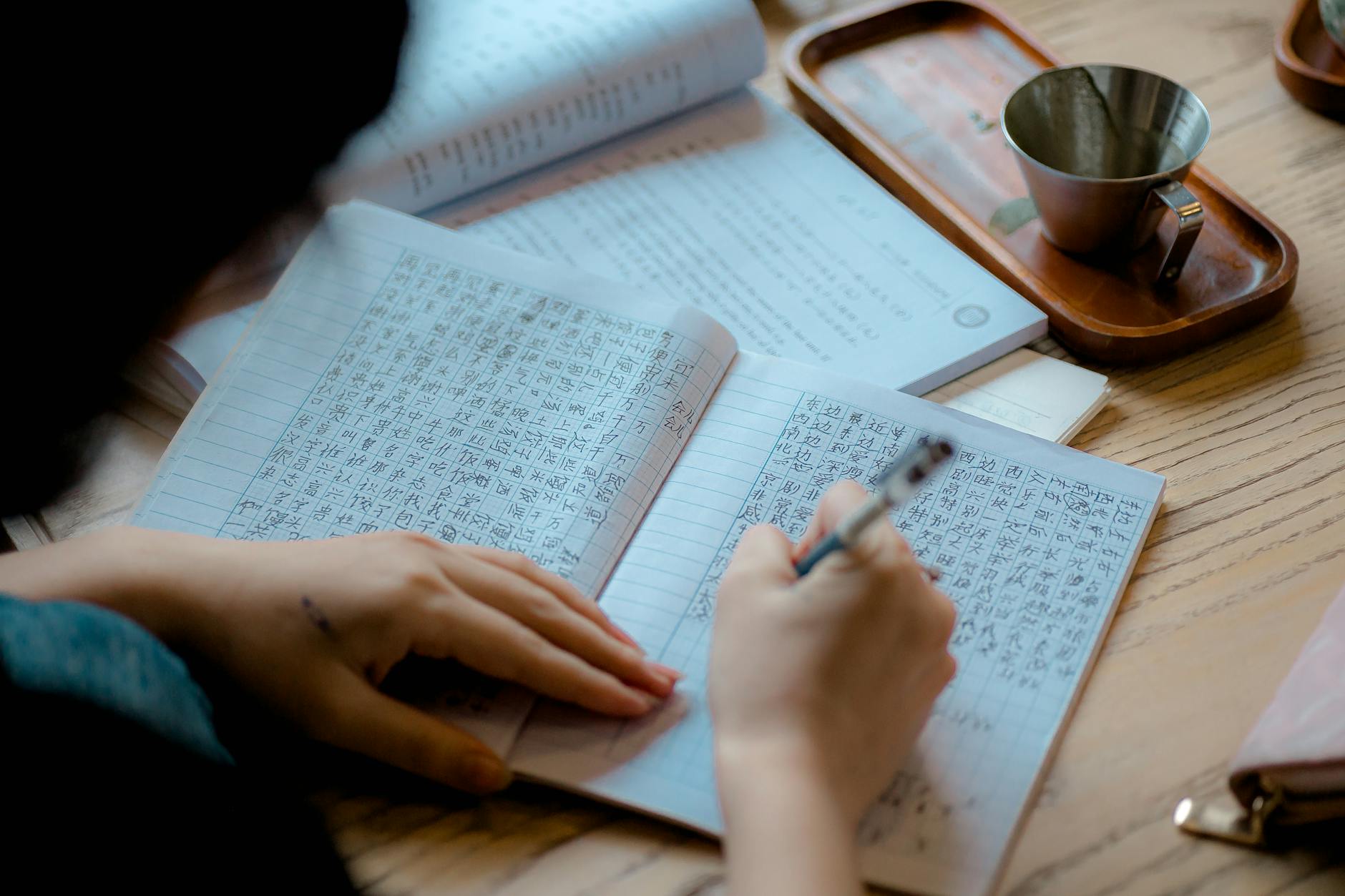 Close-up of a person writing Asian characters in a notebook indoors.