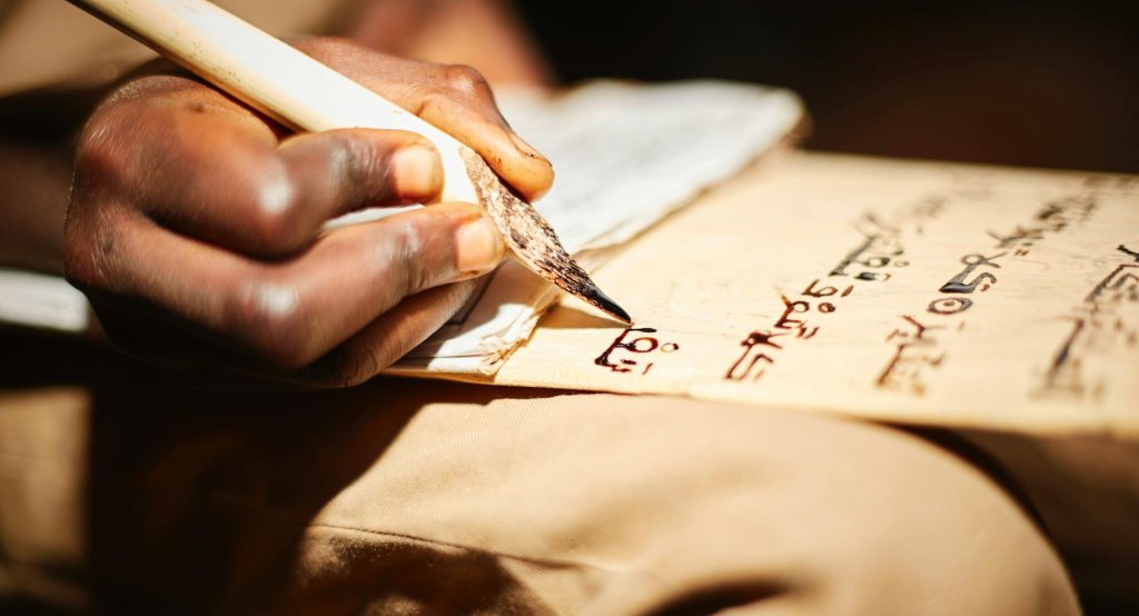 Detailed close-up of a person writing on papyrus with a traditional ink pen, highlighting cultural script.