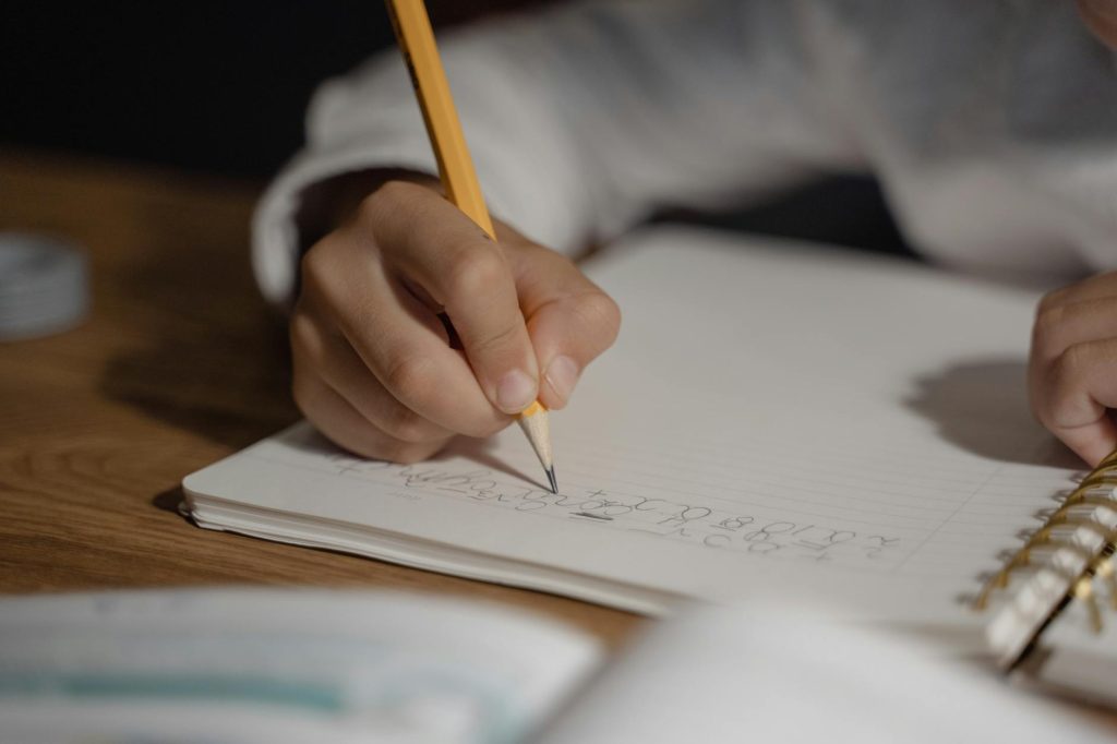 Close-up of a child writing homework using a pencil on a spiral notebook. Ideal for education themes.