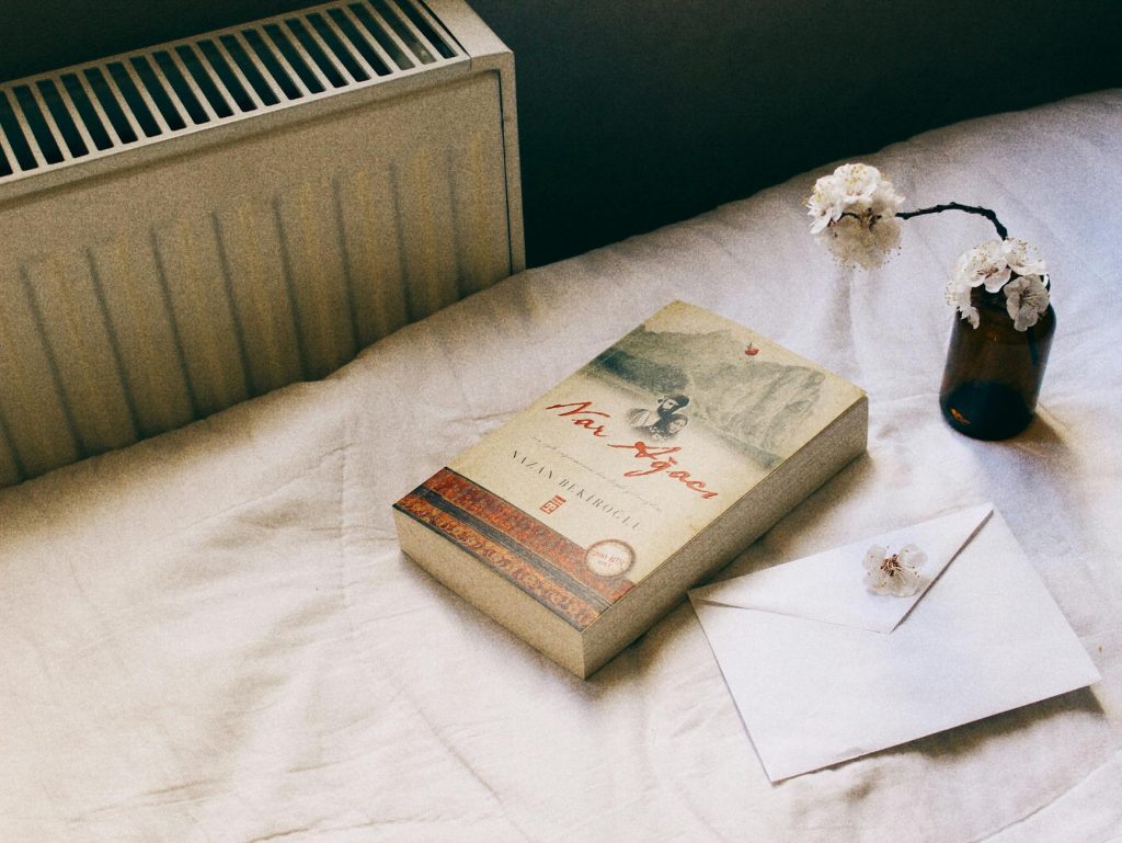 Inviting image of a book, vase with flowers, and envelope on a cozy bed setting, ideal for relaxation themes.