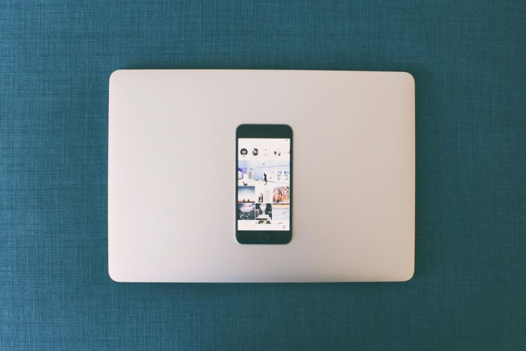 Flat lay of a smartphone on a laptop with social media photos on screen.