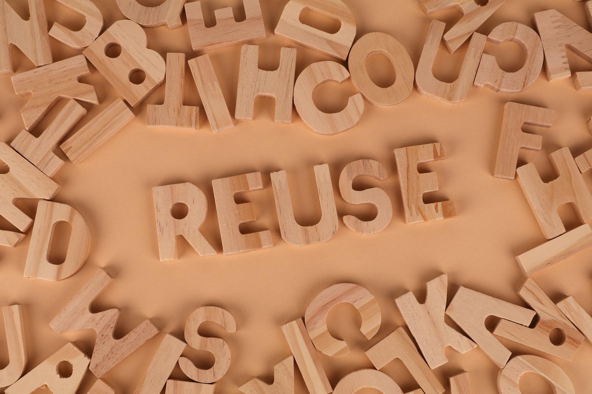 Wooden letters form the word 'Reuse' on a smooth, neutral background, symbolizing sustainability.