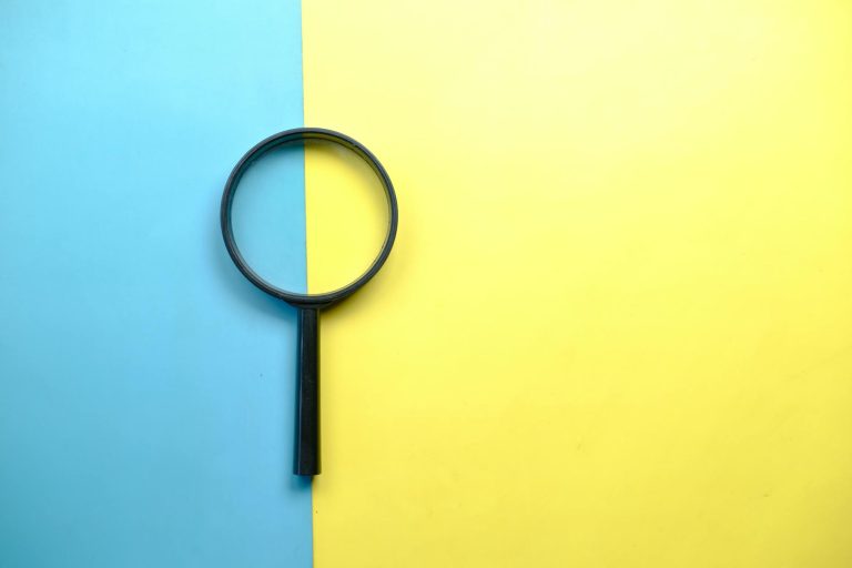 A magnifying glass lays on a split blue and yellow background in a flat lay style.