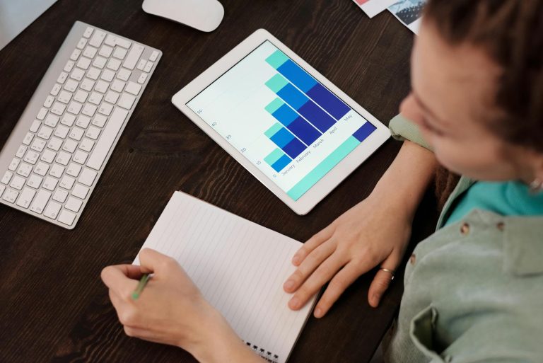 A woman taking notes while analyzing data on a tablet, ideal for business and technology themes.