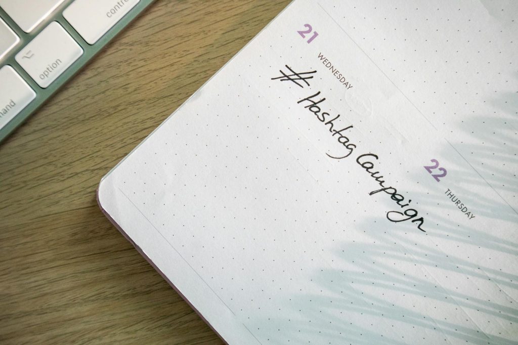 Open planner with 'Hashtag Campaign' handwritten next to keyboard. Ideal for social media and productivity themes.