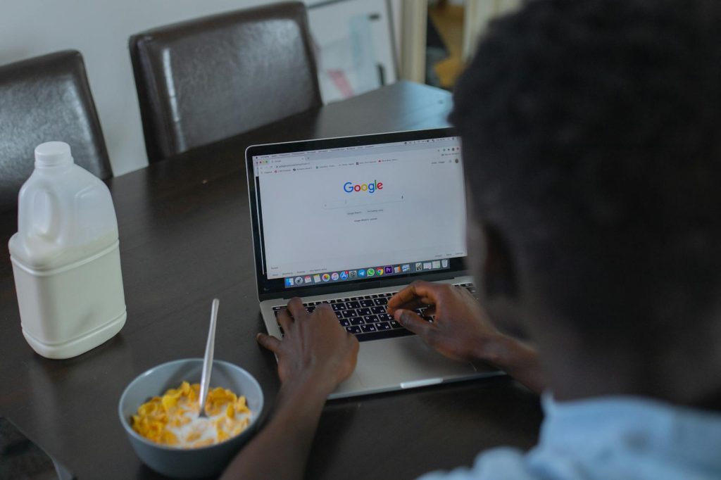 A person browsing Google on a laptop while having cereal breakfast at the table.