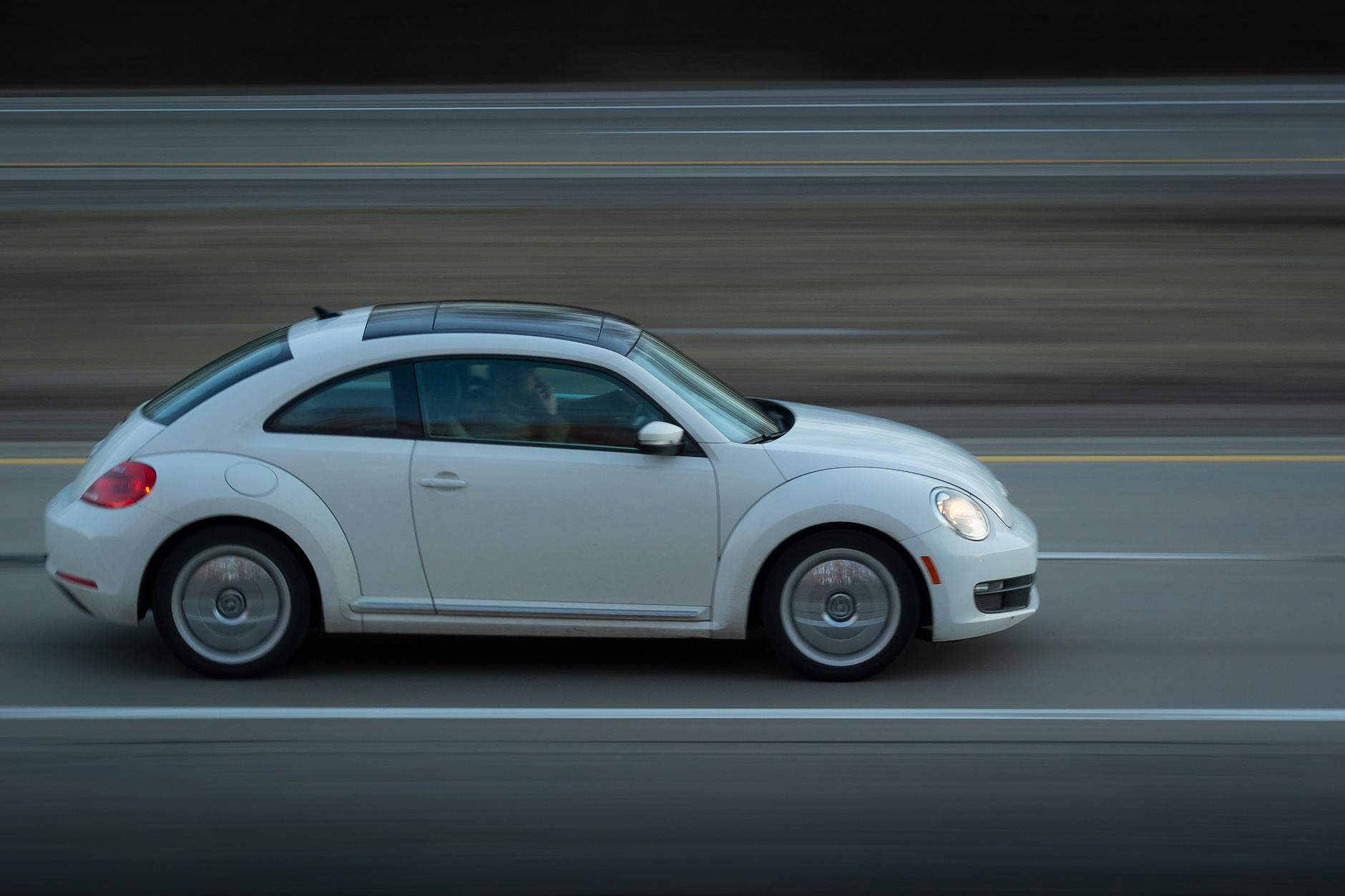 A white Volkswagen Beetle speeds along a highway, capturing motion and travel.