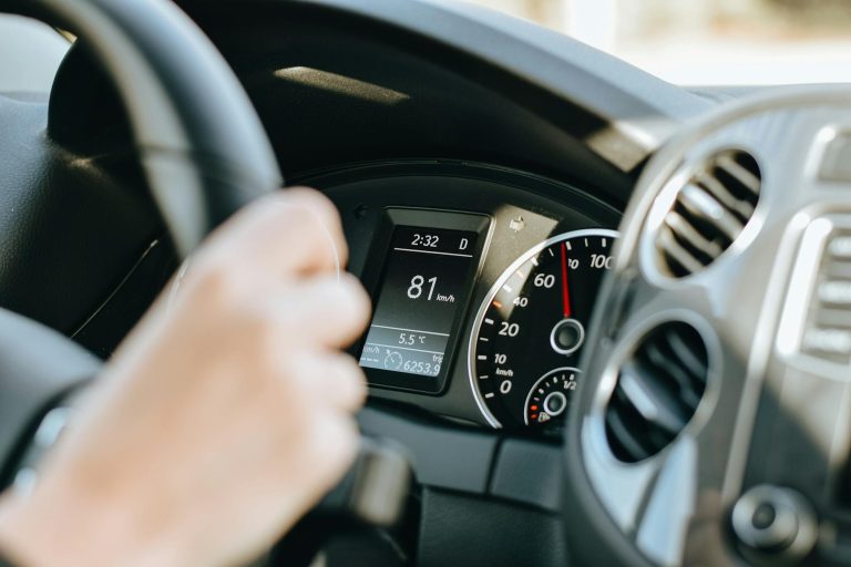 Crop anonymous person holding black steering wheel and driving car in sunny day